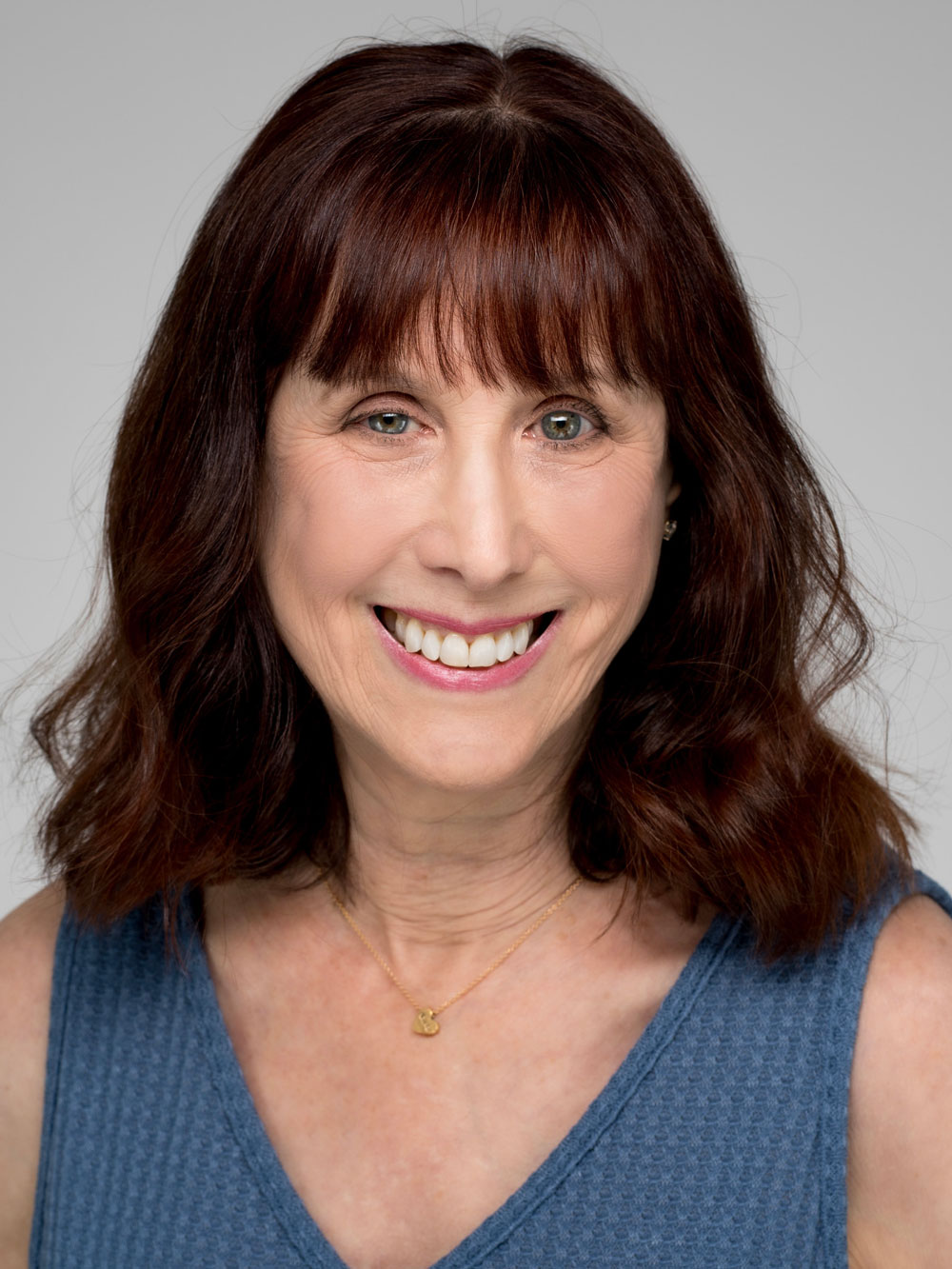 Gracie Vandiver headshot - Gracie smiles into the camera. Her chestnut hair rests on her shoulders and she wears a sleeveless blue v-neck blouse